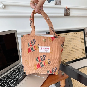 Detail of corduroy handbag with Keep Smiling print and button closure on a wooden desk
