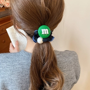 Détail d'un élastique en tissu coréen avec breloque en résine m verte et perle sur queue de cheval