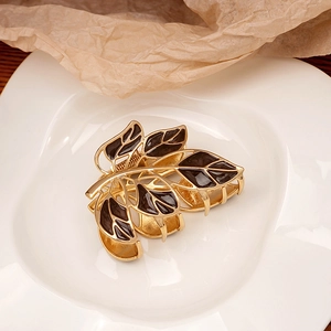 Detail of leaf-shaped gold hair claw clip with dark enamel finish on a ceramic plate