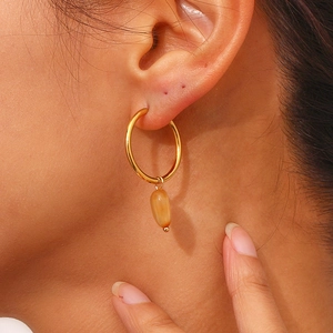 Close-up of a gold hoop earring with an amber resin teardrop pendant on the ear