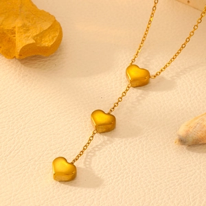 Gros plan du collier avec pendentifs cœur dorés sur une surface beige texturée