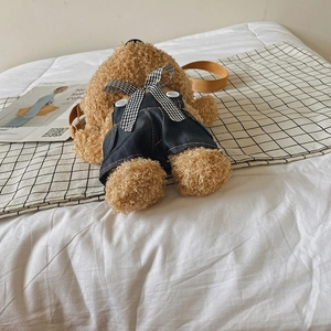 Cute teddy bear plush crossbody bag in denim overalls shown in a cozy home setting