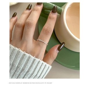 Polished silver bow ring detail shown on a hand holding a green coffee cup