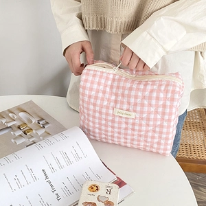 Trousse de maquillage matelassée à carreaux rose et blanc ouverte par un modèle