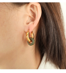 Close-up of interlocking gold-plated earrings with emerald green crystals on model