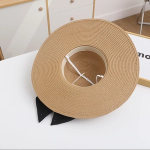 Detail showing the straw hat's interior weaving, windproof strap, and black bow ribbon
