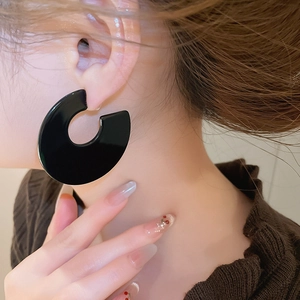 Detail view of large black acrylic C-shaped geometric hoop earrings on model