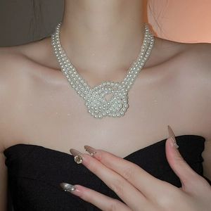 Detailed view of layered white pearl necklace with an intricate woven knot design on model