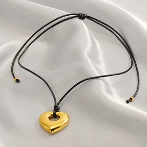 Minimalist gold heart pendant on black wax rope cord over silver silk fabric backdrop