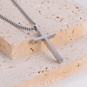 Polished silver stainless steel cross pendant on a bead chain over a beige stone