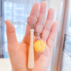 Detailed close-up of a mini wooden baseball bat and yellow ball keychain held in hand