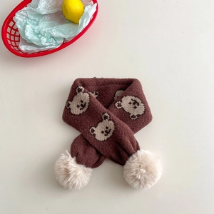 Detail of a brown knit kids scarf with bear patterns and beige faux fur pom-poms