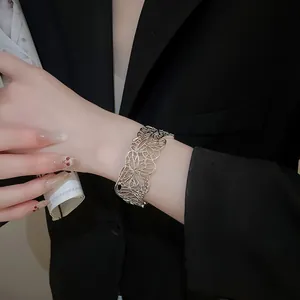 Close-up of silver hollow butterfly cuff bracelet worn on wrist with black blazer