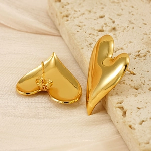 Close-up of golden 18K stainless steel heart-shaped stud earrings on a beige stone base