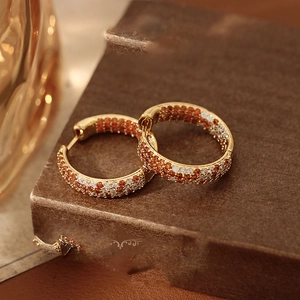 Macro detail of gold huggie earrings with orange and white pave-set zircons