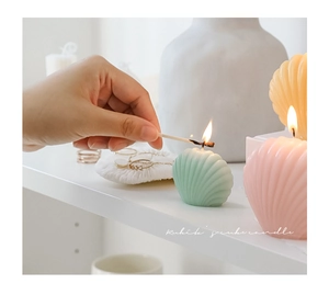 Lighting a mint green shell-shaped scented candle with a match in a home setting
