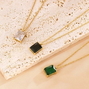Close-up of three gold necklaces with rectangular clear, black and emerald glass pendants