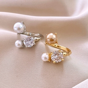 Detailed view of gold and silver open rings with pearls and sparkling zircon on satin