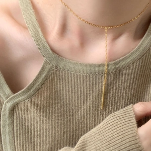 Close-up of a minimalist gold bar necklace worn on a textured olive green knit sweater