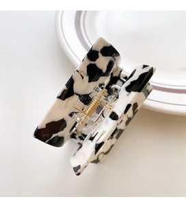 Detail of square hair claw clip with black and white cow pattern and gold spring