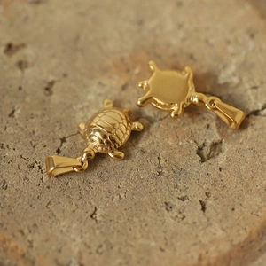 Macro shot of two golden turtle pendants in titanium steel on a natural stone surface