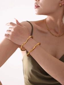 Detail showing two stacked irregular wavy gold bangles on a model wrist in polished finish