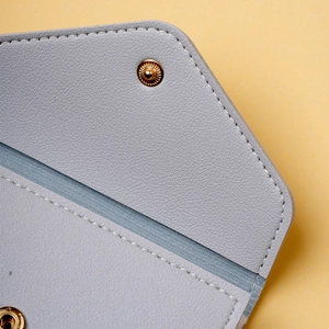 Detailed close-up of blue lychee grain leather wallet with a golden metal snap button