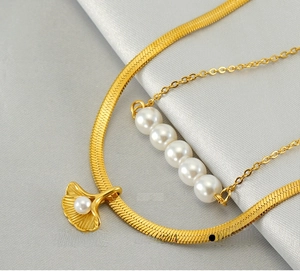 Detail of 18K gold layered necklace featuring ginkgo leaf pendant and white pearls