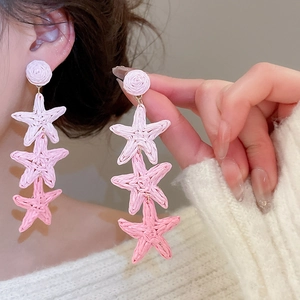 Close-up of handmade pink gradient raffia star tassel earrings worn by model