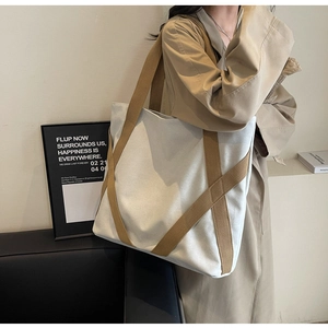 Detailed shot of a beige canvas tote bag with brown straps styled with a trench coat