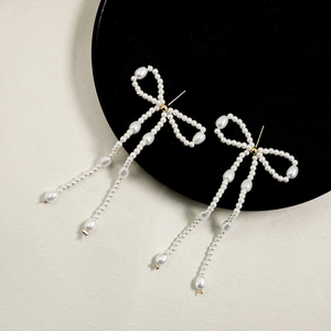 Detail shot of long tassel pearl bow earrings with golden studs on a black tray