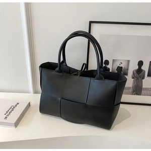 Detail of black woven leather tote bag with sturdy handles on a minimalist white desk