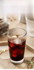 Close-up of vertical ribbed glass cup with coffee and ice on a wooden tray