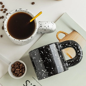 Modern ceramic ink-splatter mugs with chunky handles and golden spoon on white table