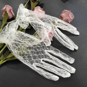 Detailed view of white floral lace gloves with ruffled wrist trim on a dark grey surface