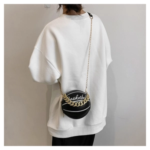 Black round basketball purse with white patterns and gold chain shown on a model