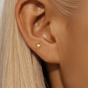 Close-up of a gold flower stud earring with a central zircon on a model's ear lobe