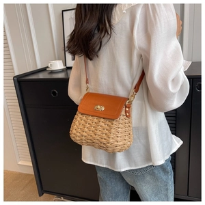 Detail of hand-woven straw crossbody bag with orange leather flap and gold lock worn by model