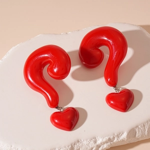 Macro shot of red resin question mark earrings with heart pendants on a textured stone base