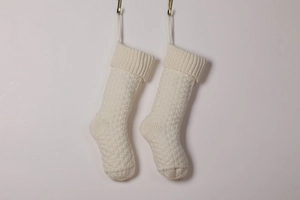 Pair of off-white knitted Christmas stockings with diamond patterns hanging on hooks