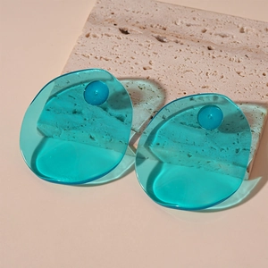 Macro view of translucent blue resin oval earrings on a natural textured stone surface