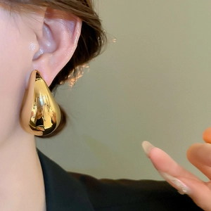 Close-up of a polished gold teardrop earring with a high-shine metallic finish on model