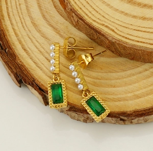 Detail of square green zircon earrings with white pearls on a natural wood surface