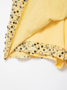 Close-up of yellow wrap skirt with decorative silver and black sequins on the hemline
