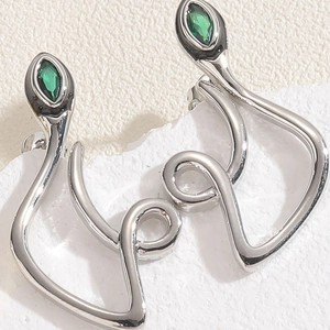 Macro shot of silver snake earrings with marquise green stones on white marble base
