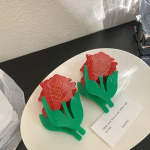 Red rose hair claw clip with green leaves and gold outlines in a white ceramic dish
