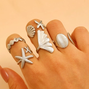 Close-up of ocean-themed starfish and seashell rings layered on finger in silver finish