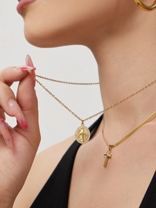 Detail of layered gold goddess medallion and cross pendant necklace set on model