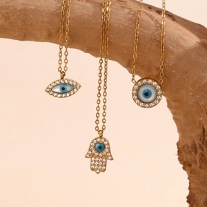 Détail de colliers œil maléfique et main de Fatma plaqués or sur une branche en bois