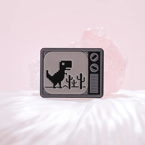 Spilla in smalto dinosauro pixel retrò su schermo TV con cactus e tocchi rosa